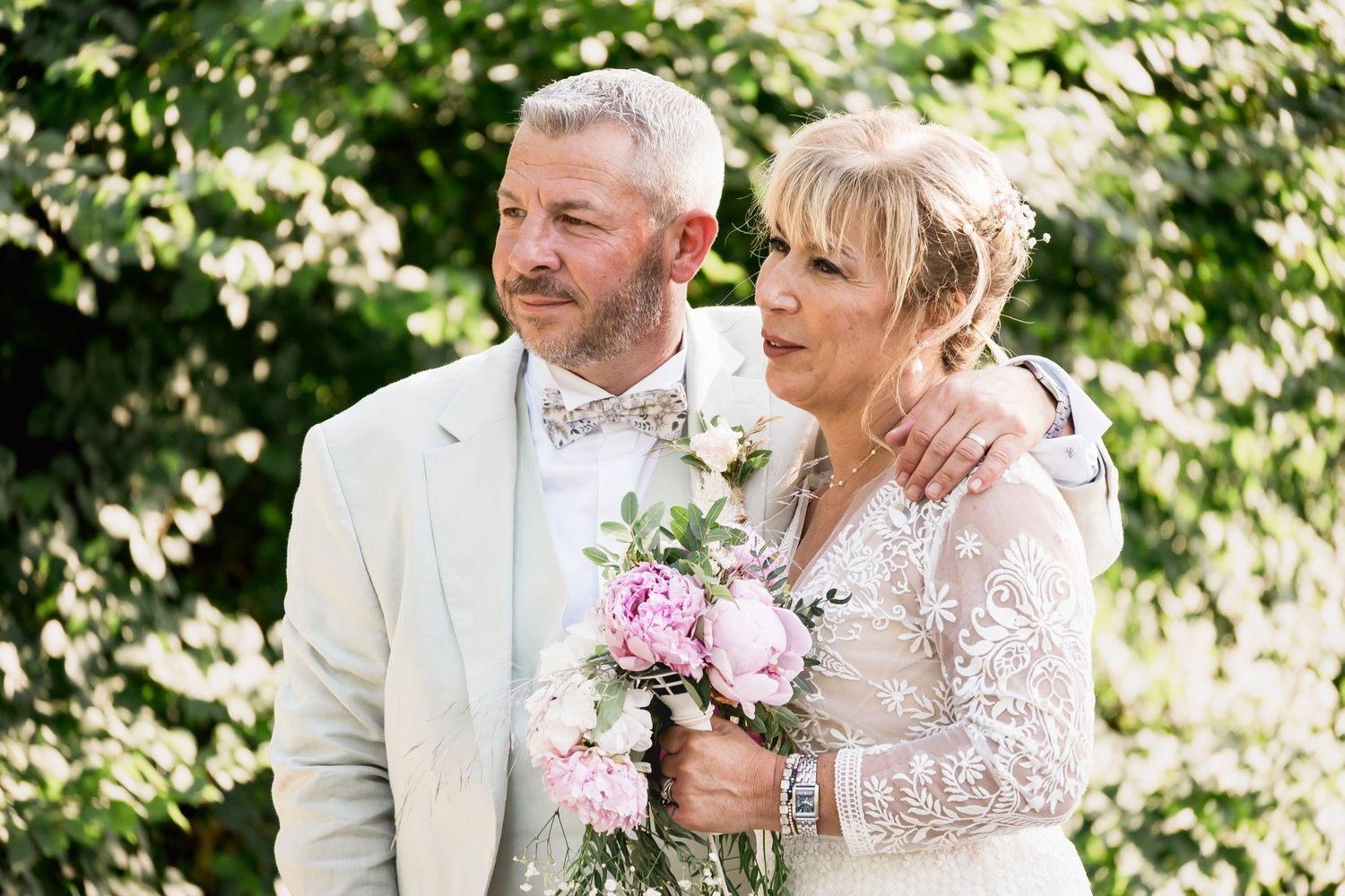 Elegant couple shares romantic wedding day moments outdoors with pink floral bouquet and white attire.