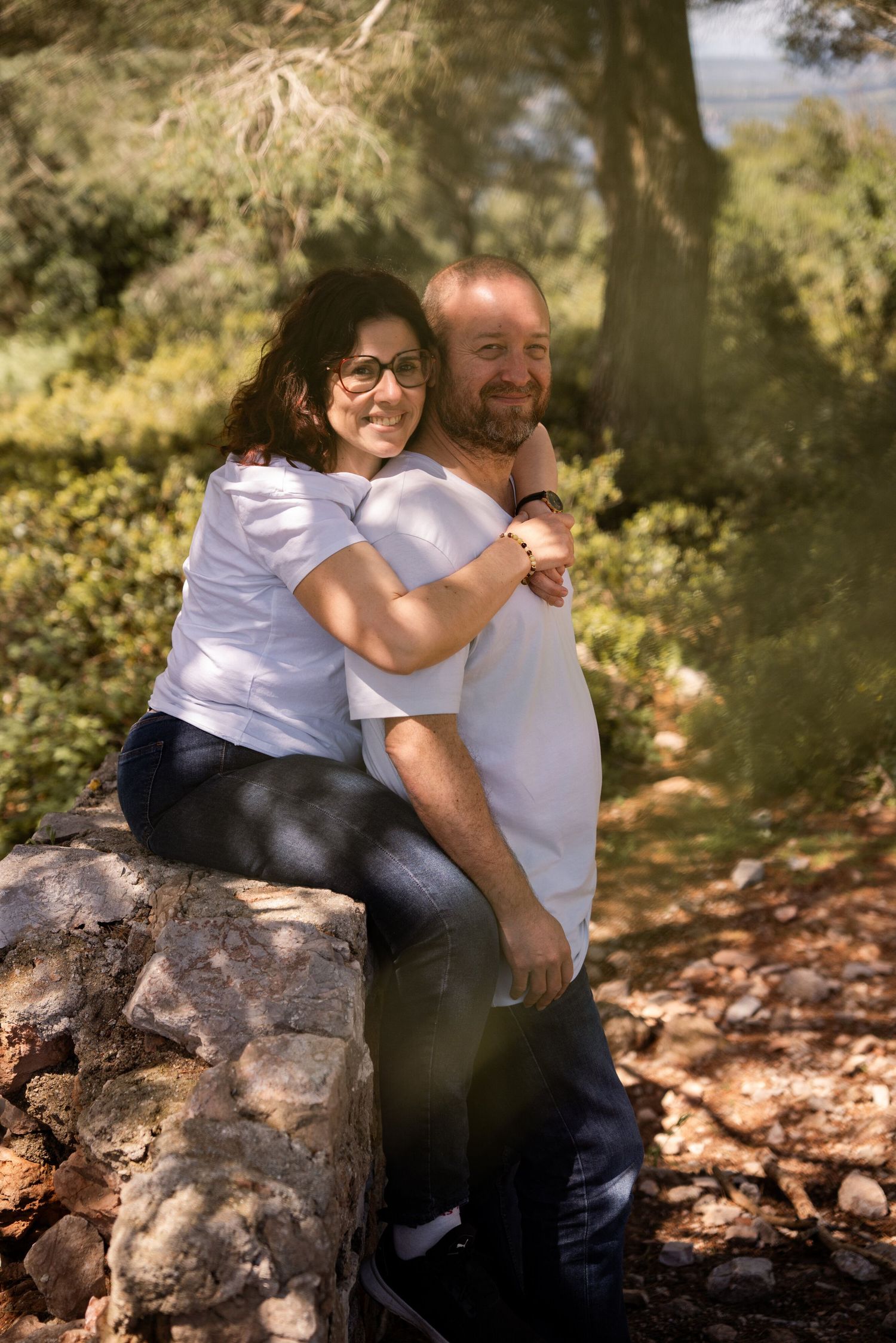 Couple sharing intimate moment while sitting on stone wall in natural setting.
