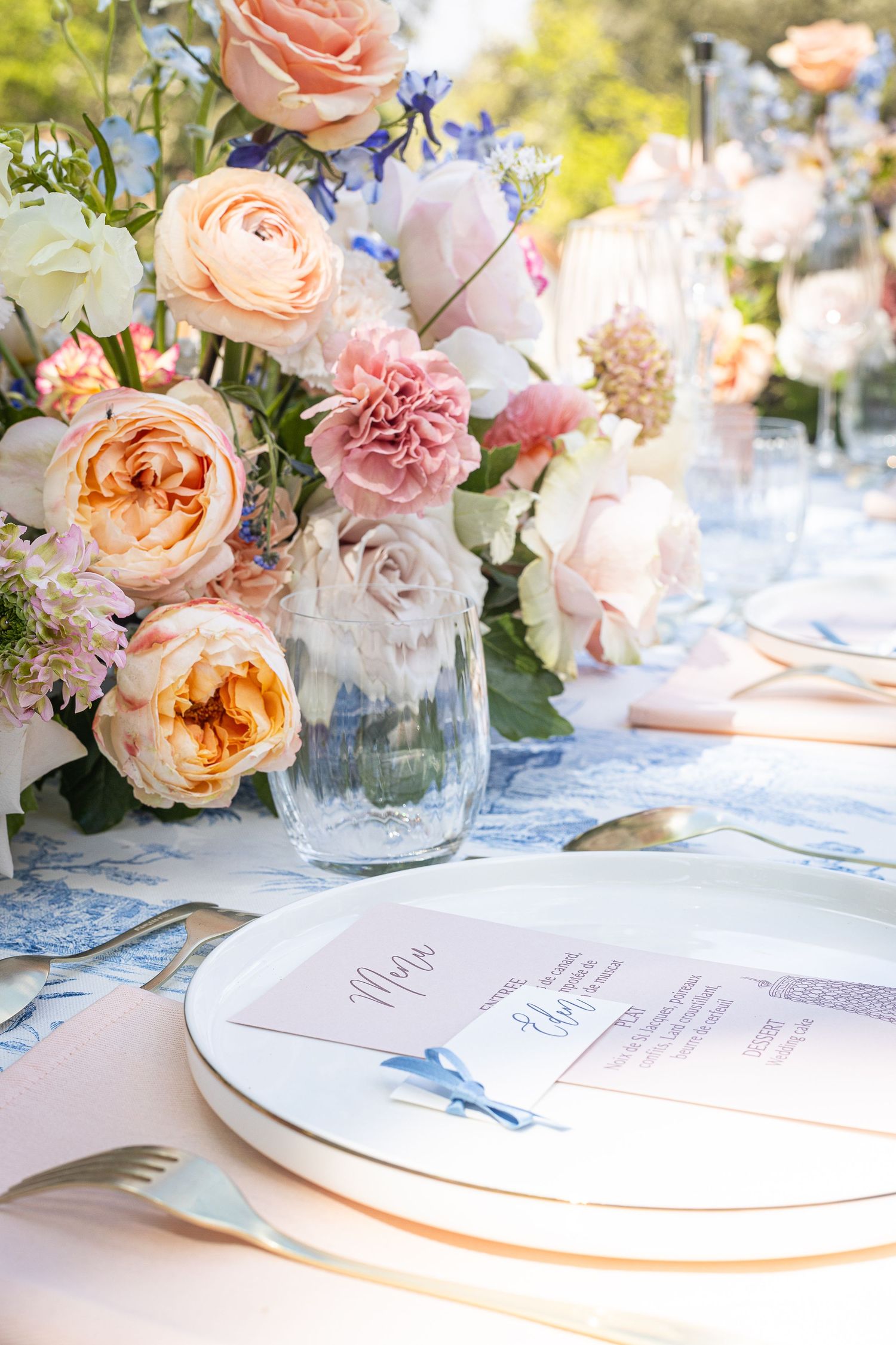 Elegant wedding table setting with peach and pink roses in glass vases and white table decor.