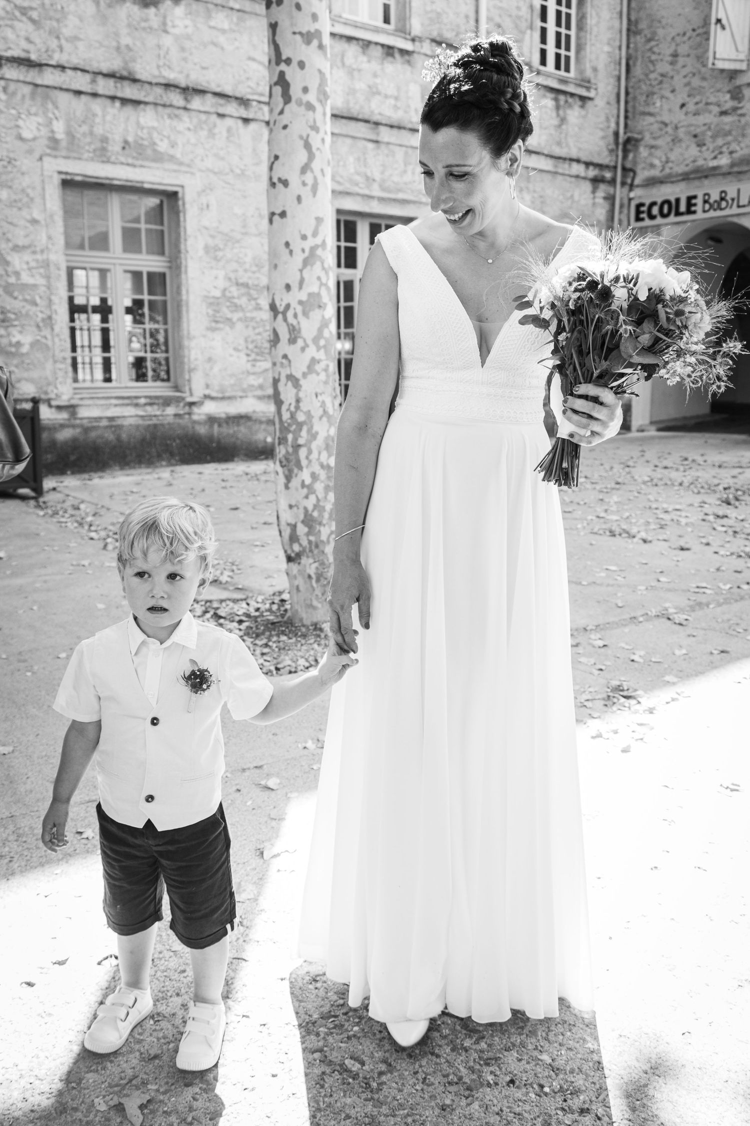 Playful outdoor wedding photos with white dresses and stone walls on a sunny day.