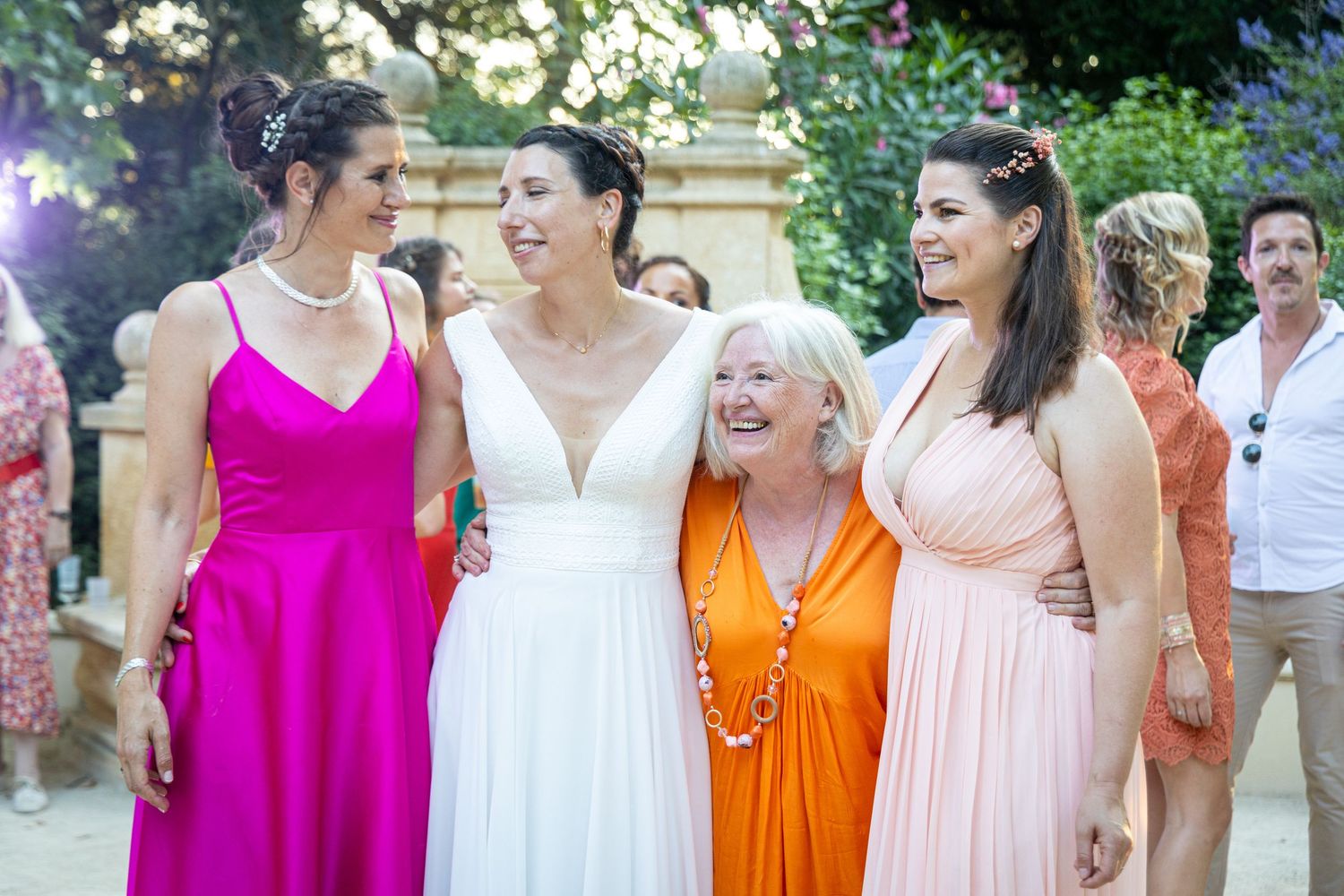 Wedding party members laughing together in colorful dresses during outdoor celebration.