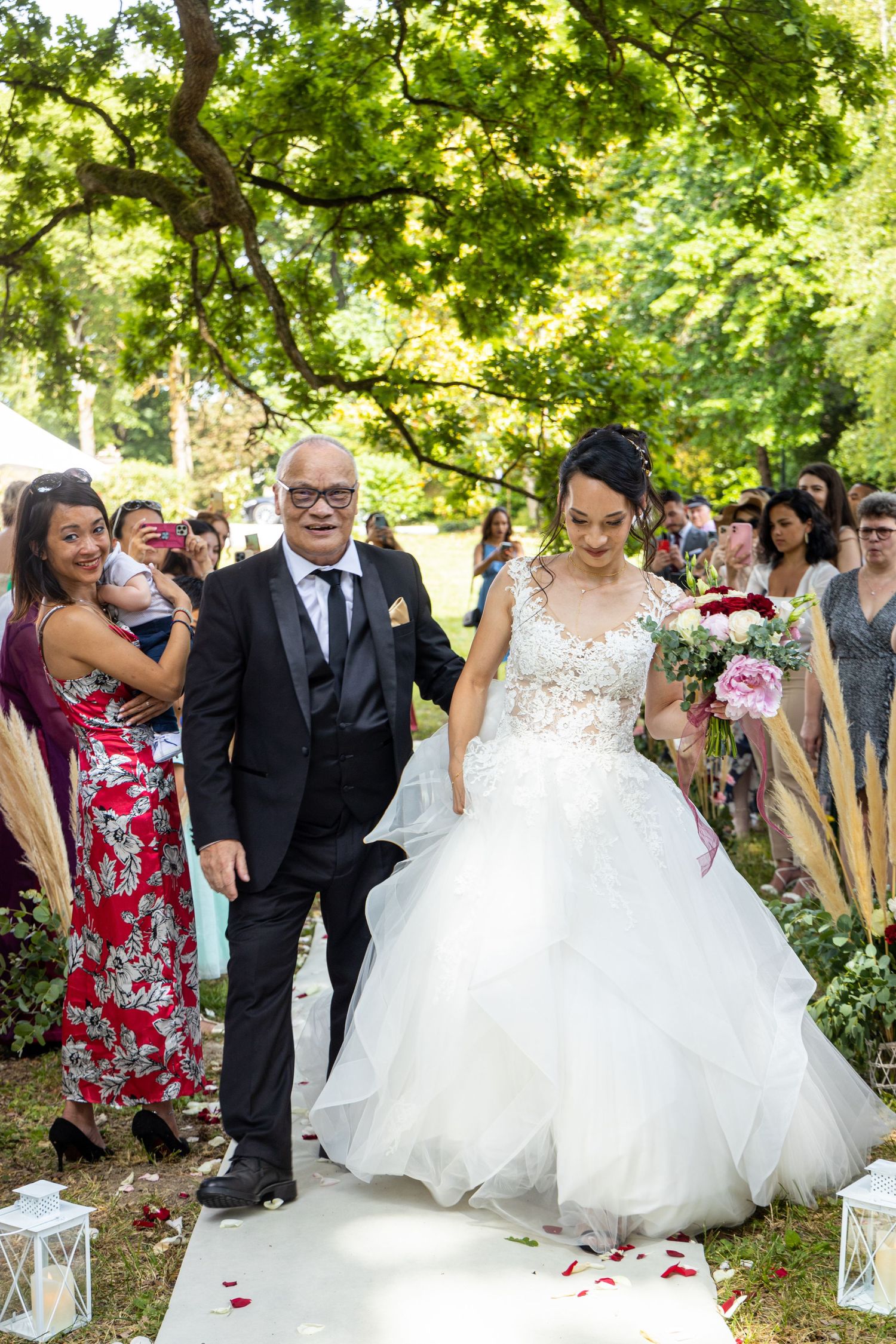 Wedding party walks down outdoor aisle decorated with lanterns and rose petals.