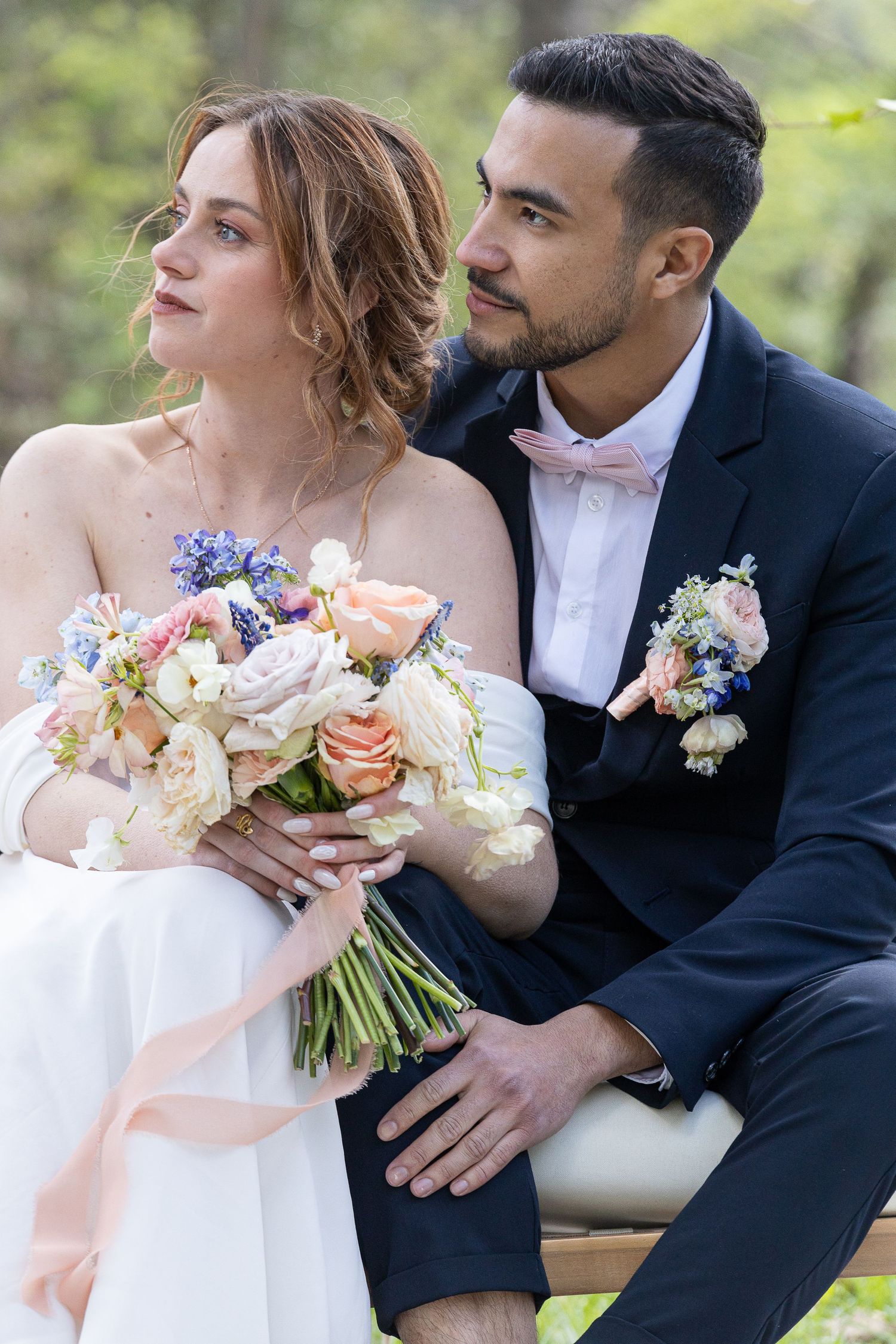 Wedding couple poses with elegant pastel bouquet featuring roses and wildflowers.