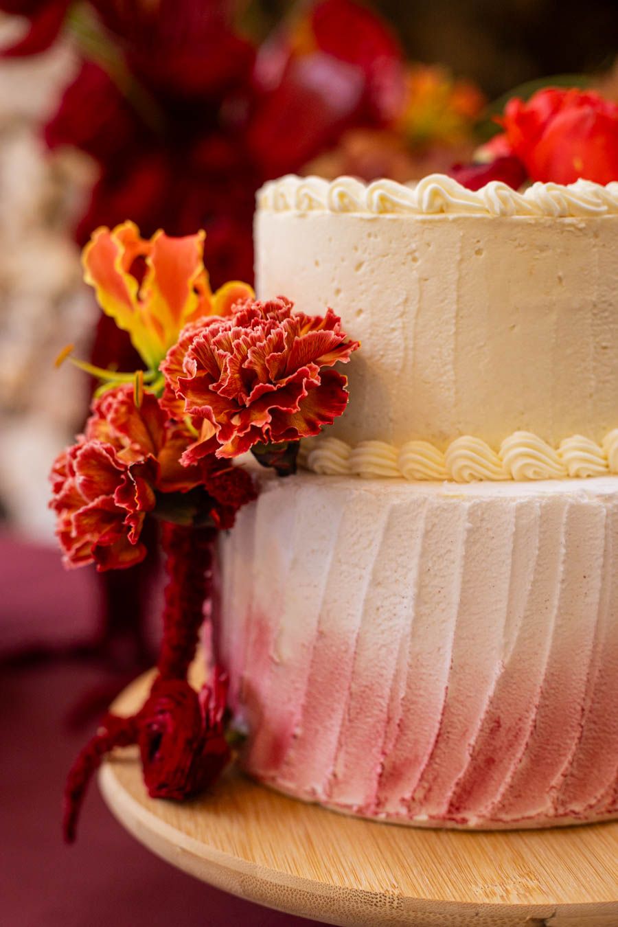 Two-tiered white wedding cake decorated with red and orange carnations.