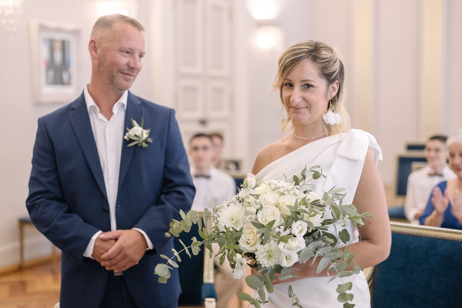 Wedding party members stand in formal attire with white floral bouquets.