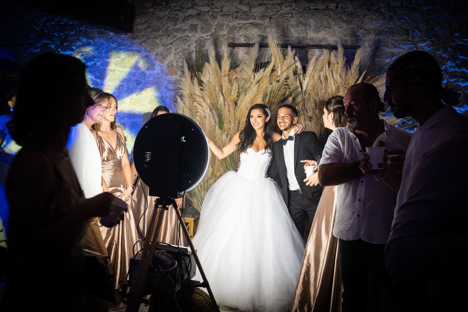 Wedding party celebrates in an evening reception with balloons and wheat decor against blue lighting.