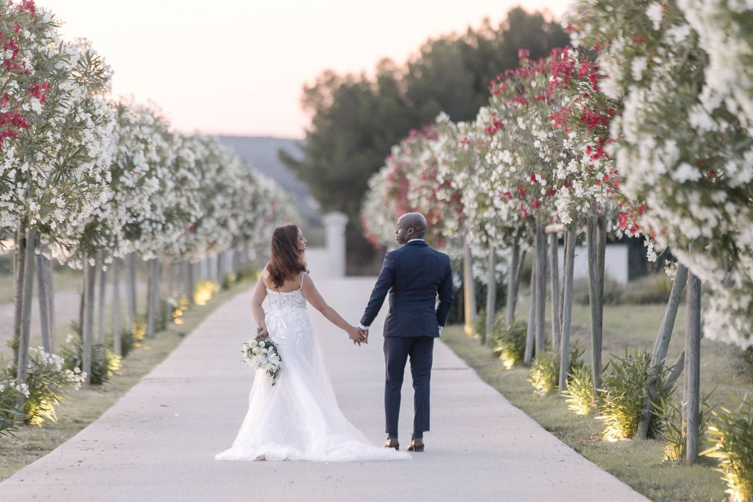 Couple walks through a beautiful garden path lined with blooming trees.