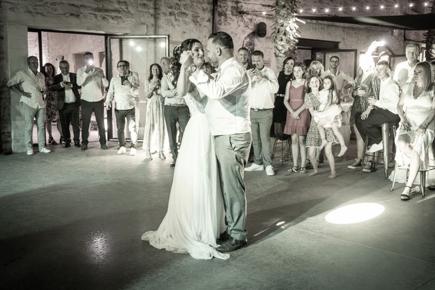 Wedding party dances and celebrates on outdoor patio under string lights.