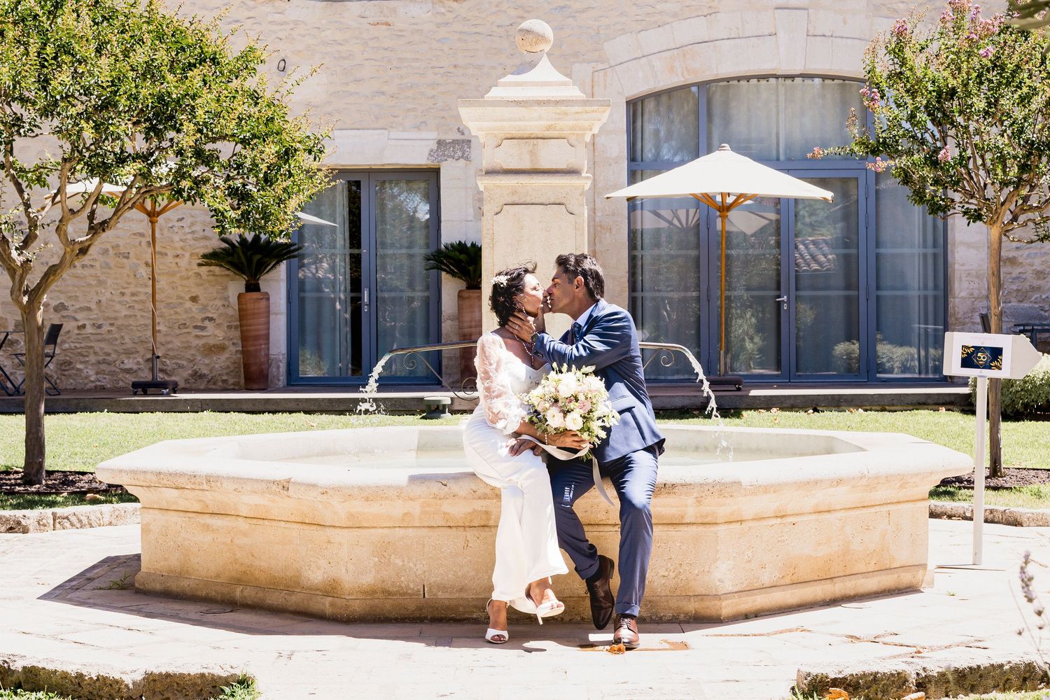 A couple poses outdoors near a stone building wall while celebrating their wedding day.