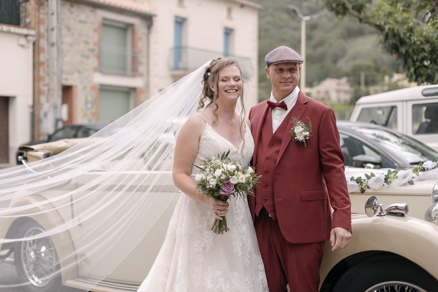 Wedding couple walking outside with flowing veil and burgundy attire.