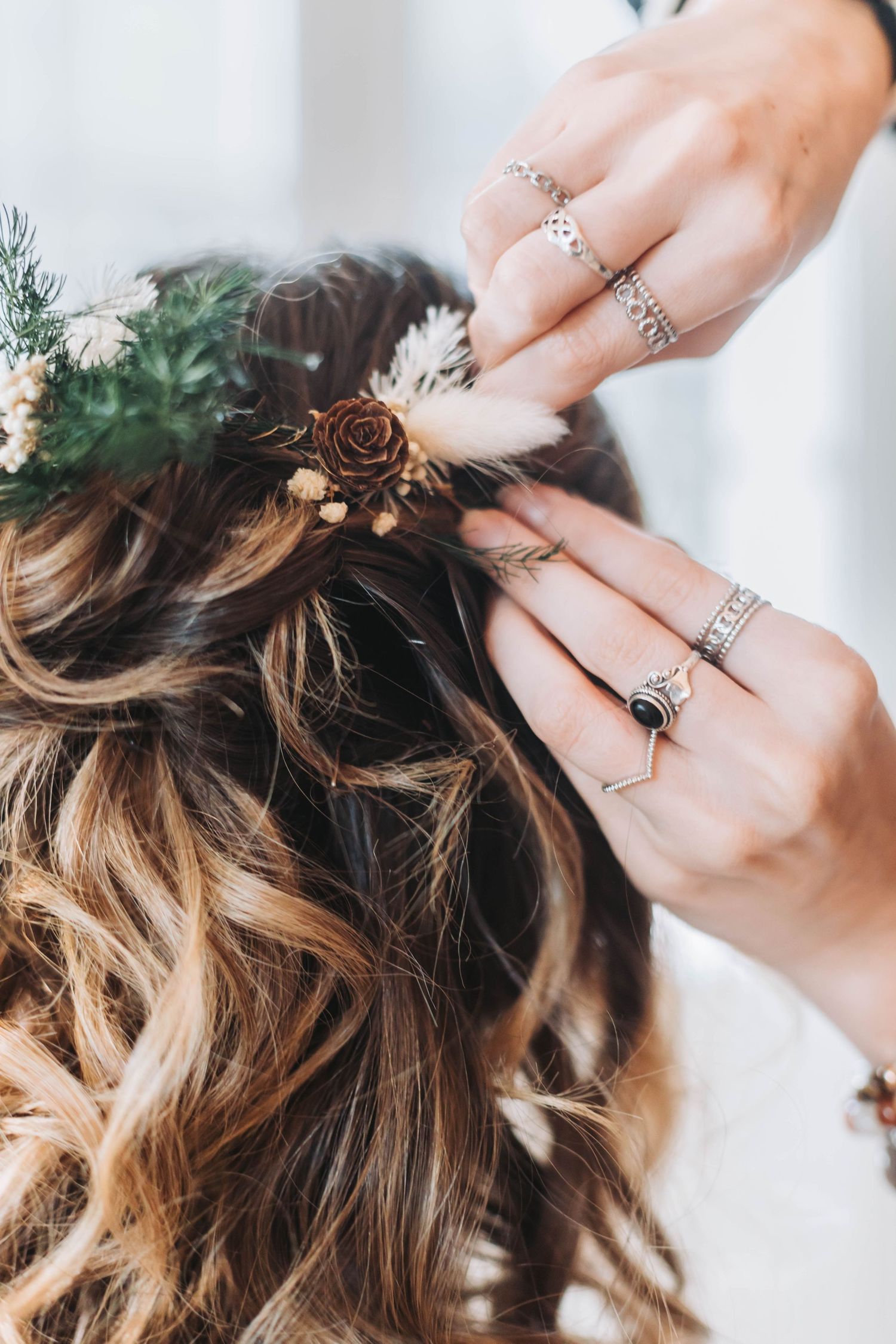 Close-up of hands styling hair with delicate floral accessories and jewelry.