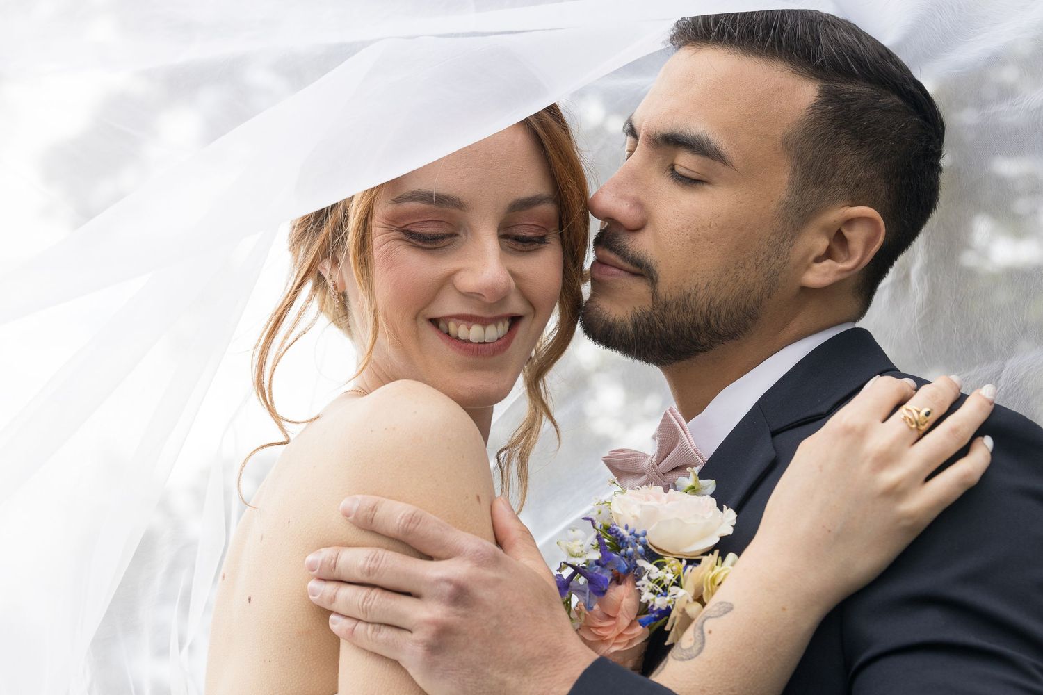 Intimate wedding portrait of couple embracing with bride's veil flowing.
