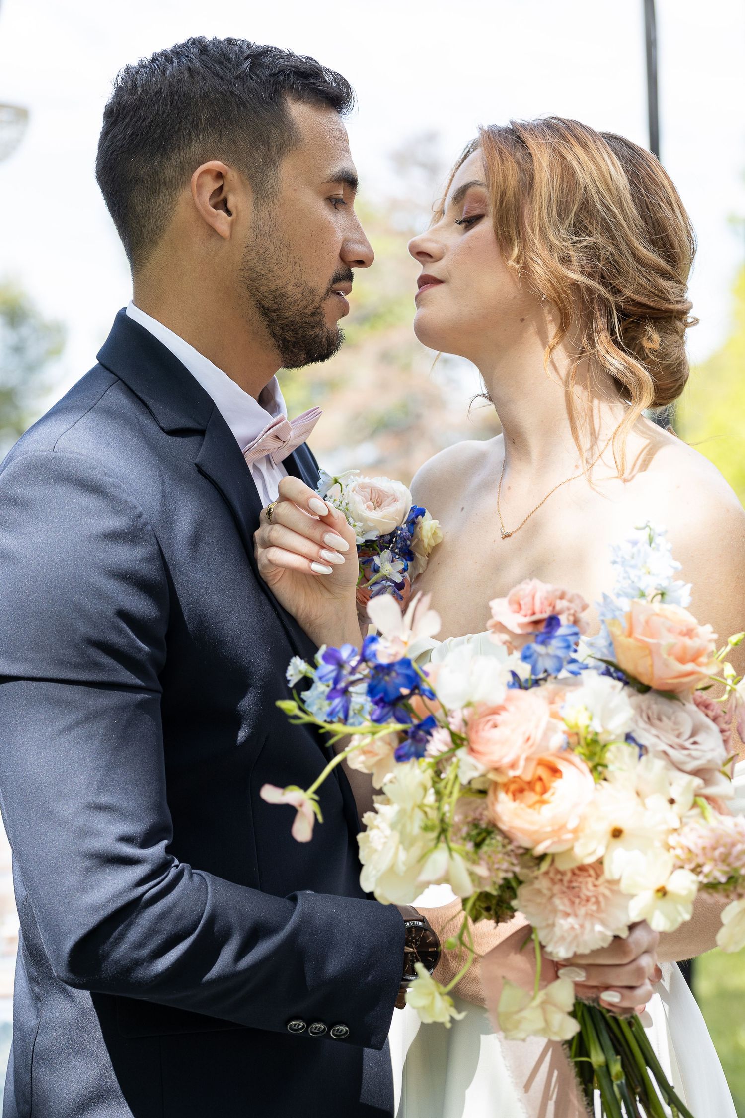 Romantic wedding couple embracing while bride holds a beautiful bouquet of peach and blue flowers.