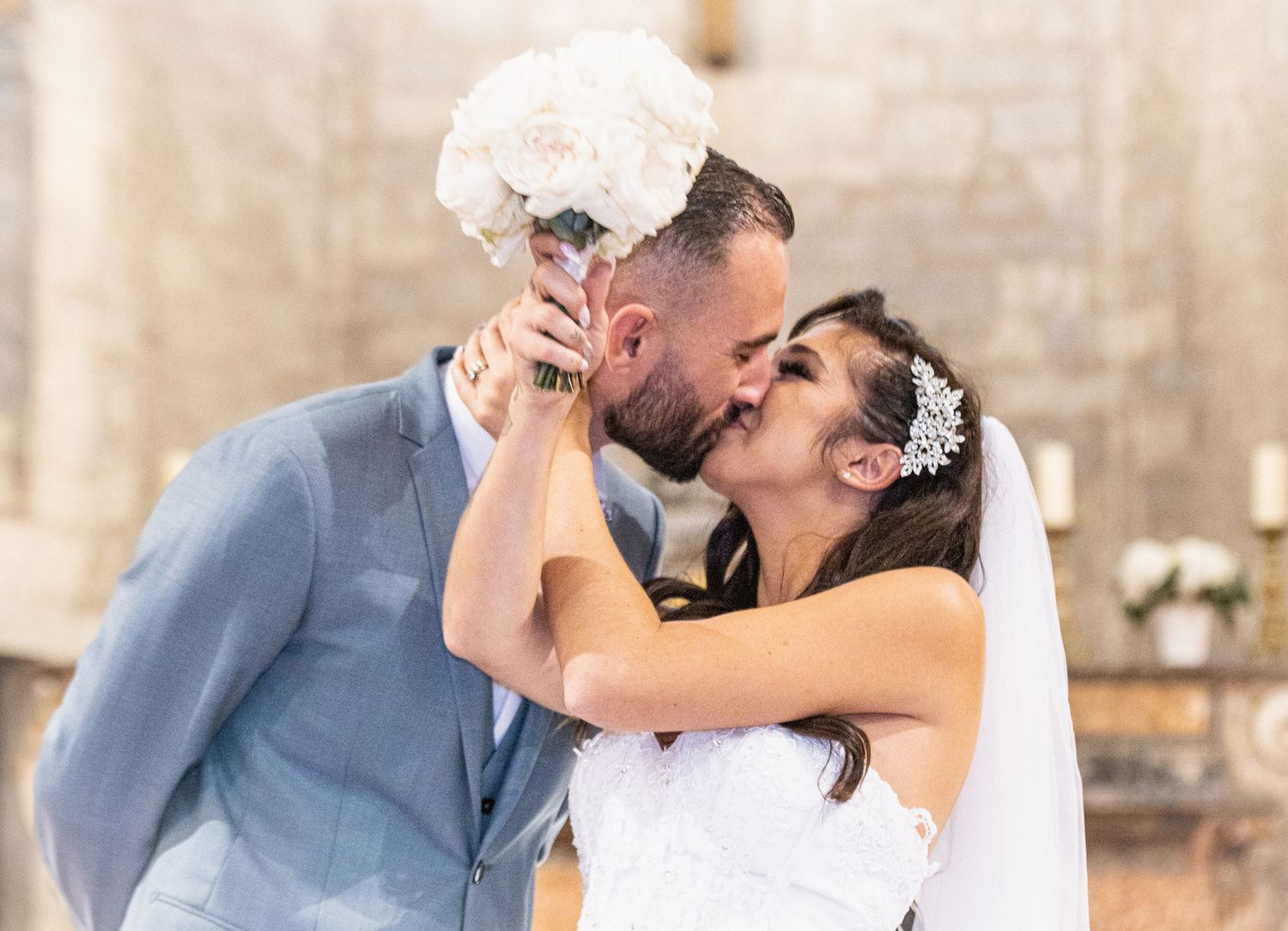 A romantic wedding moment captured as couple shares a kiss with white bouquet raised.