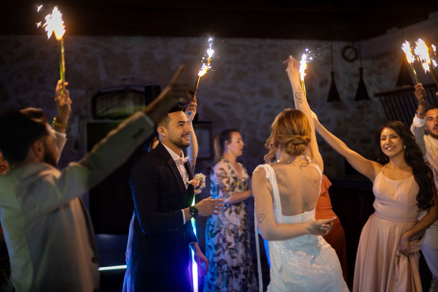 Wedding guests dancing and celebrating with sparklers at a nighttime reception.