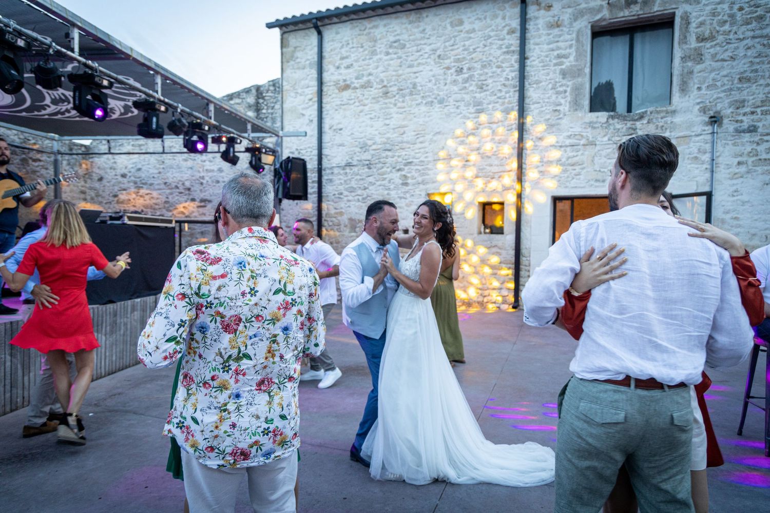 Wedding celebration with guests dancing outside a rustic stone building.