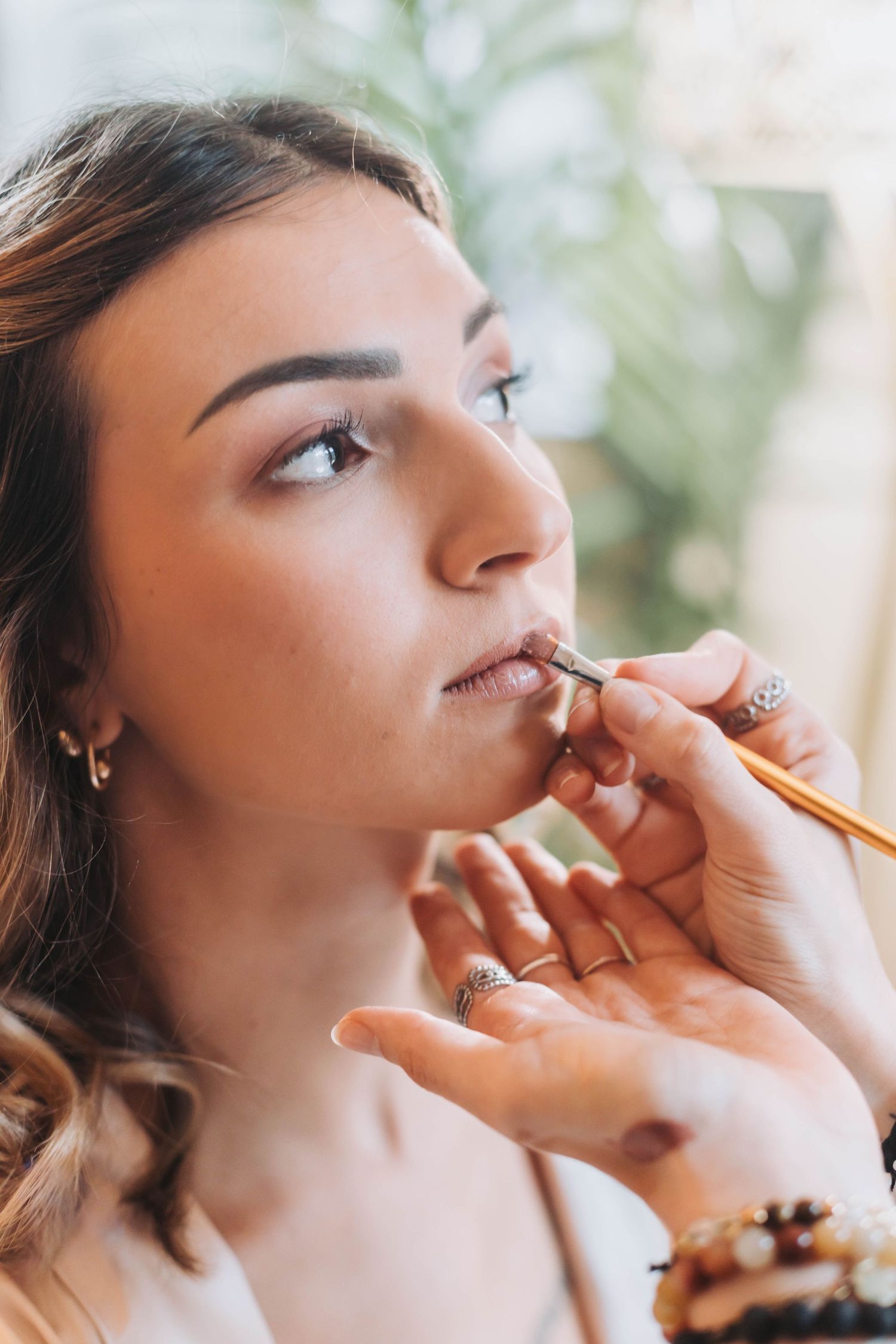 Professional makeup artist applying lip color during bridal preparation with soft natural lighting.
