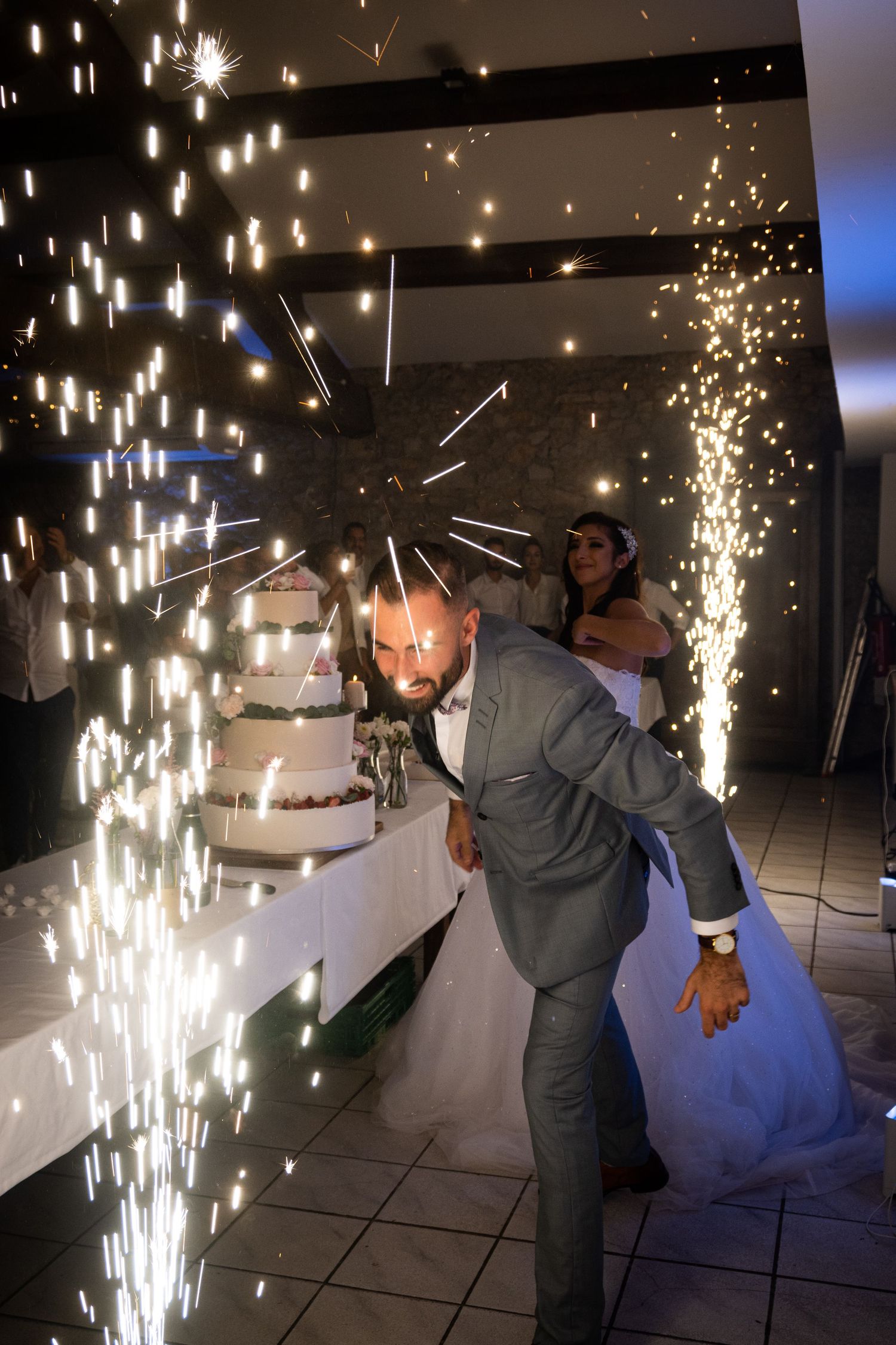 Wedding cake cutting moment illuminated by dramatic indoor sparklers and lighting effects.