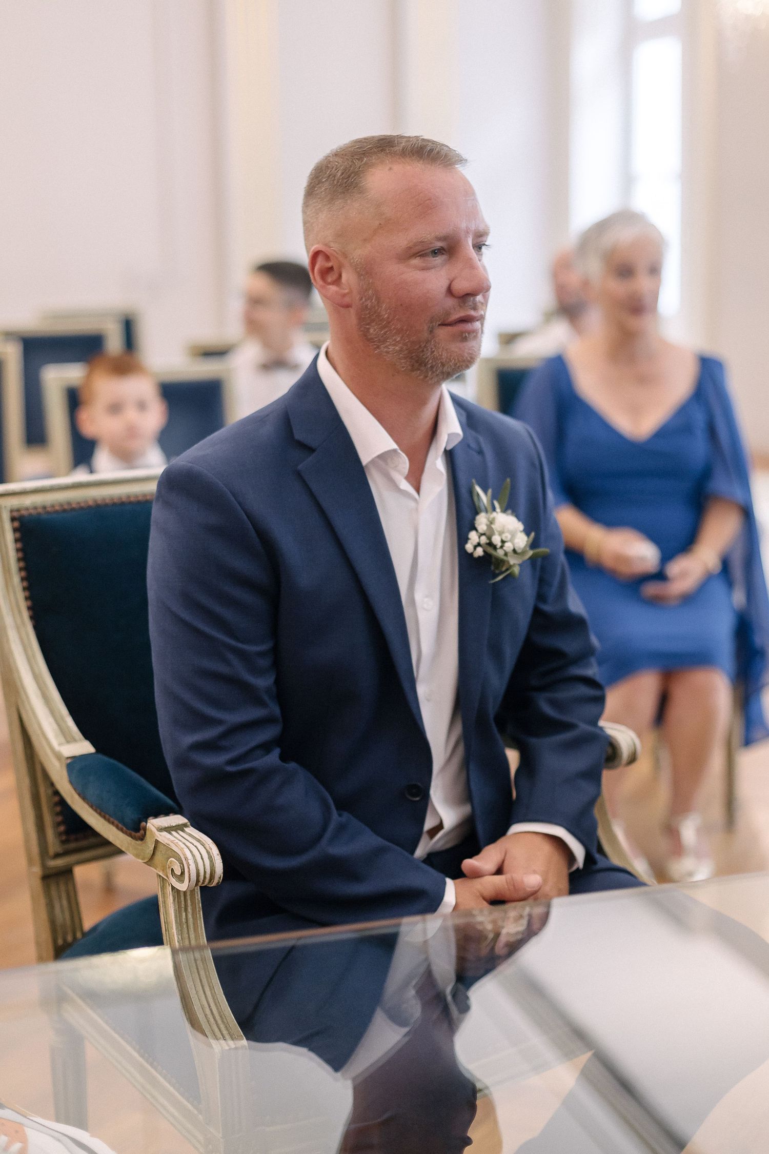 Guests in formal attire seated in elegant chairs during wedding ceremony.