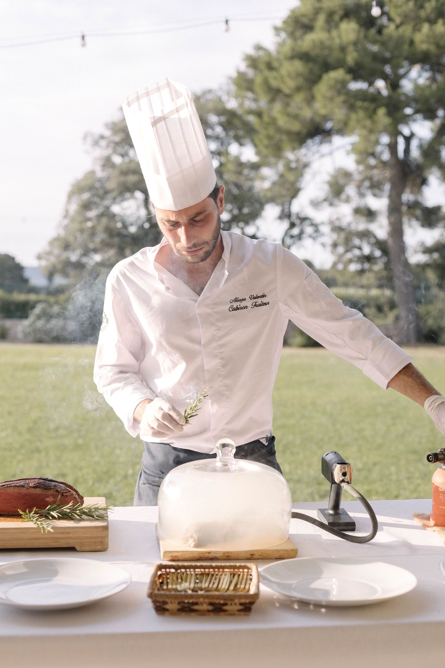 Chef in white uniform plating and preparing elegant dishes in a professional kitchen setting.
