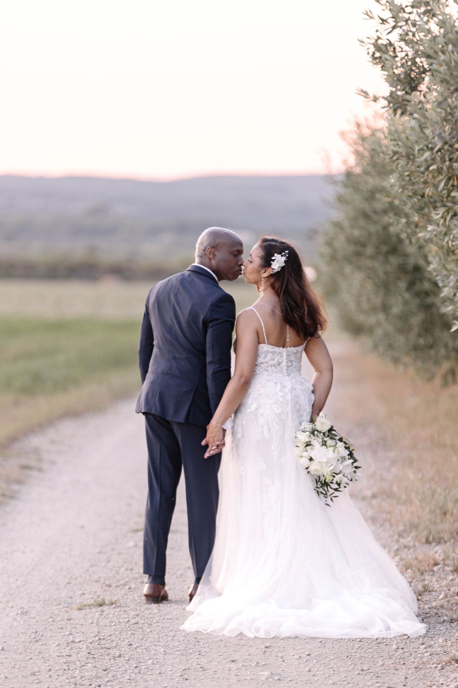 Newlyweds walk hand in hand down a winding country path at dusk.