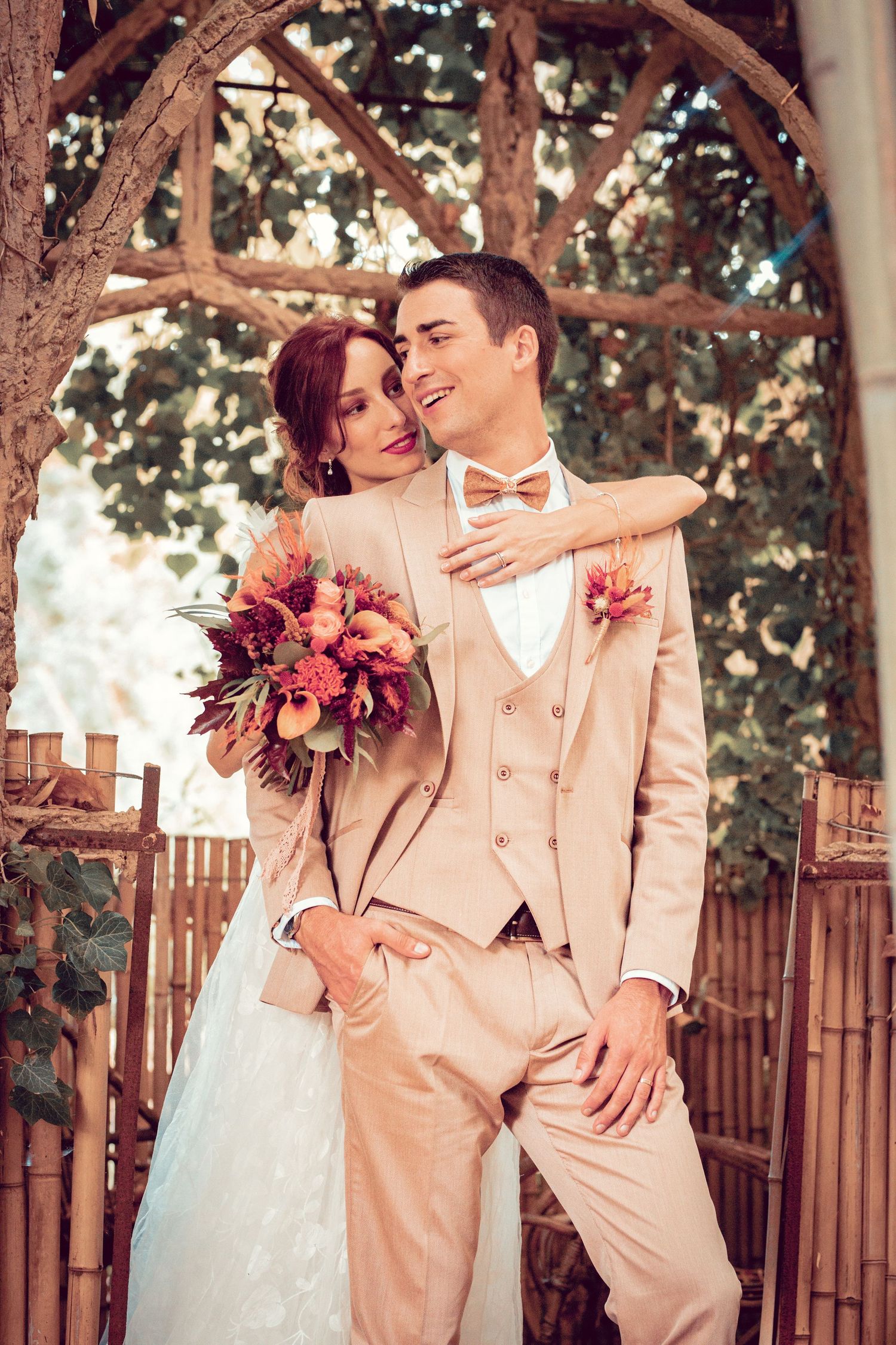 Wedding couple embraces under rustic wooden archway in garden setting.