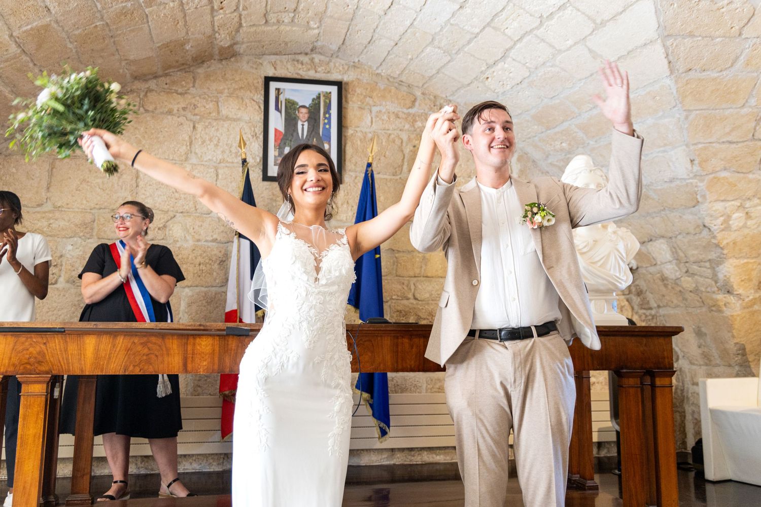 Newlyweds celebrate with raised arms in stone church during joyful ceremony.