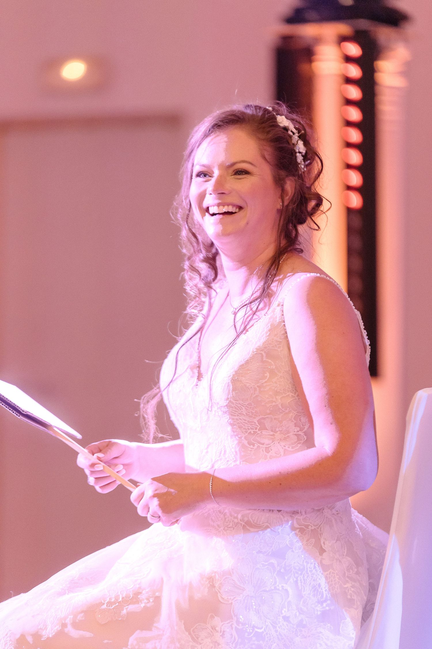 A joyful bride in white lace dress smiling while seated during wedding celebrations.