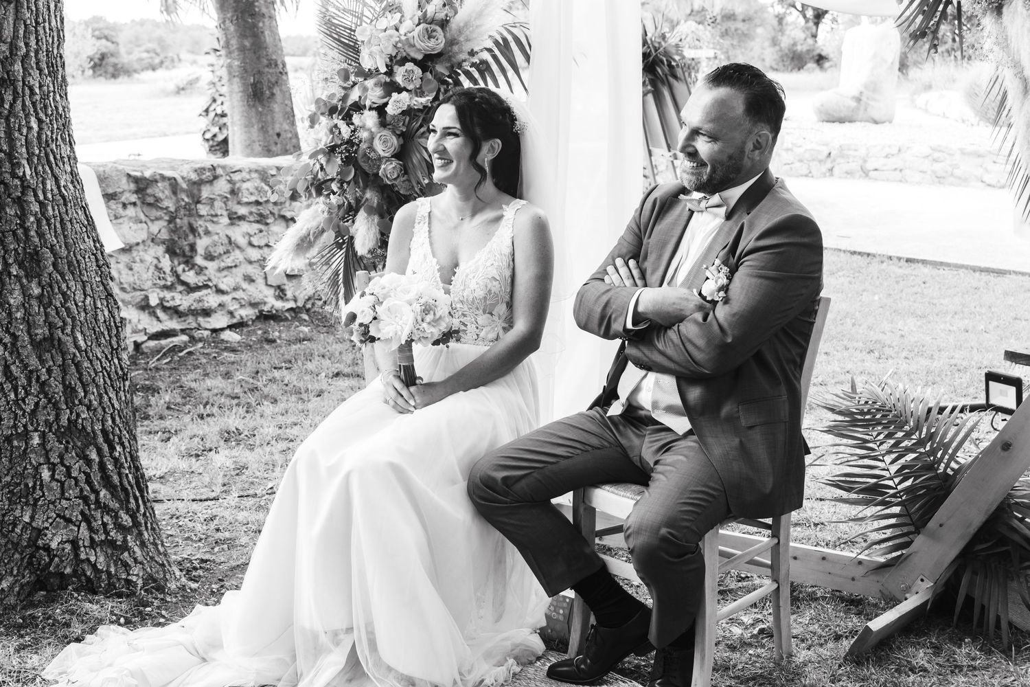 Black and white photo of a wedding ceremony taking place in a natural outdoor setting under trees.