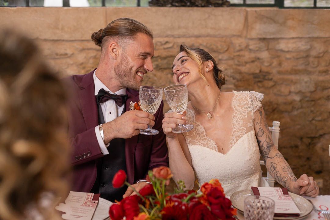 Wedding couple sharing an intimate moment at a rustic reception with stone walls and red floral decor.
