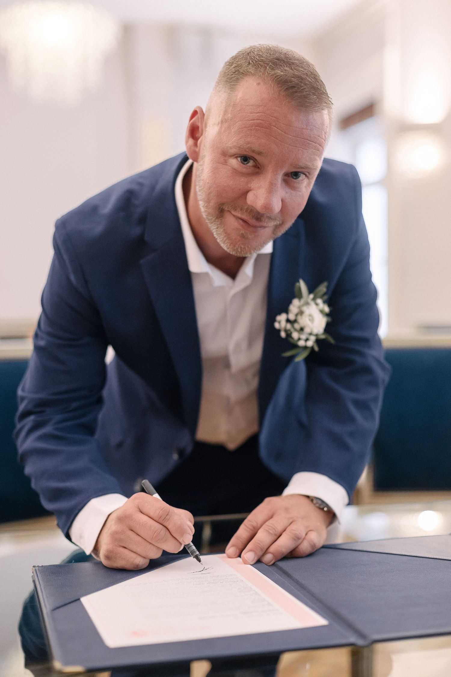 Groom in navy suit signs marriage certificate during wedding ceremony.