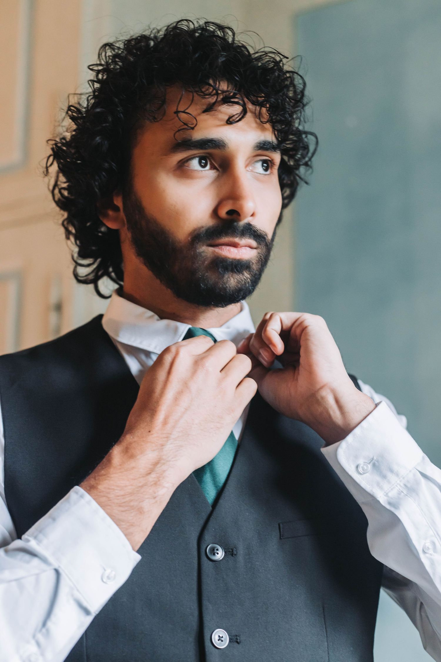 Groom adjusts his tie while wearing a formal dark vest and white shirt.