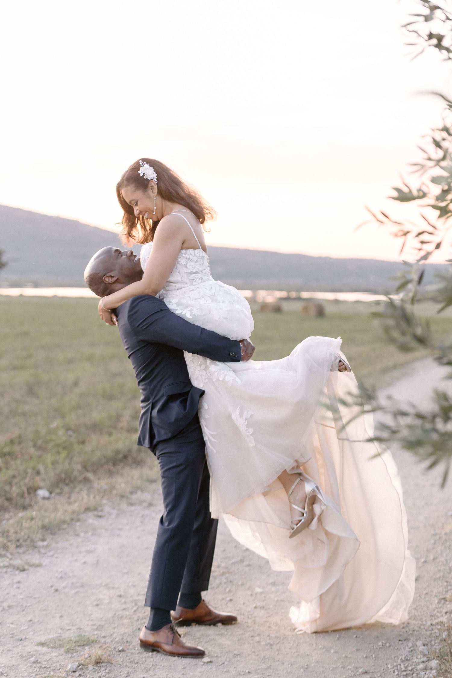 Dramatic sunset wedding portrait with groom lifting bride in flowing white dress.