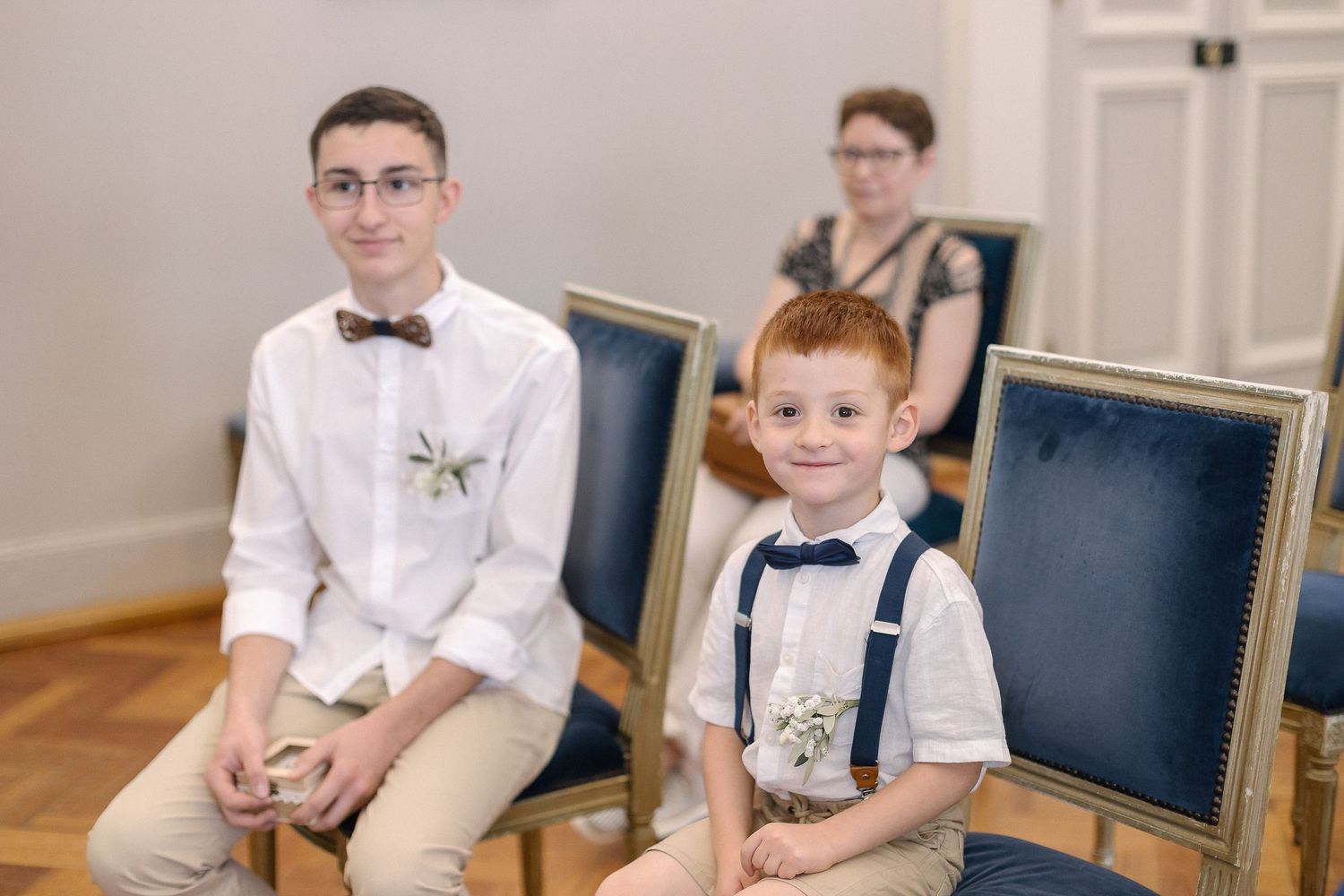 Young ring bearers in white shirts and khakis sit patiently in navy chairs during ceremony.