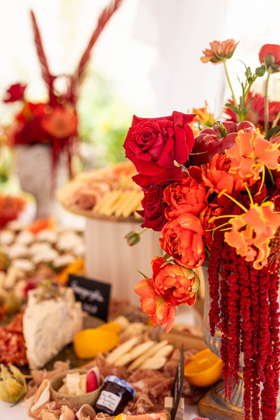 Red and orange floral centerpiece with roses and charcuterie spread at wedding reception.