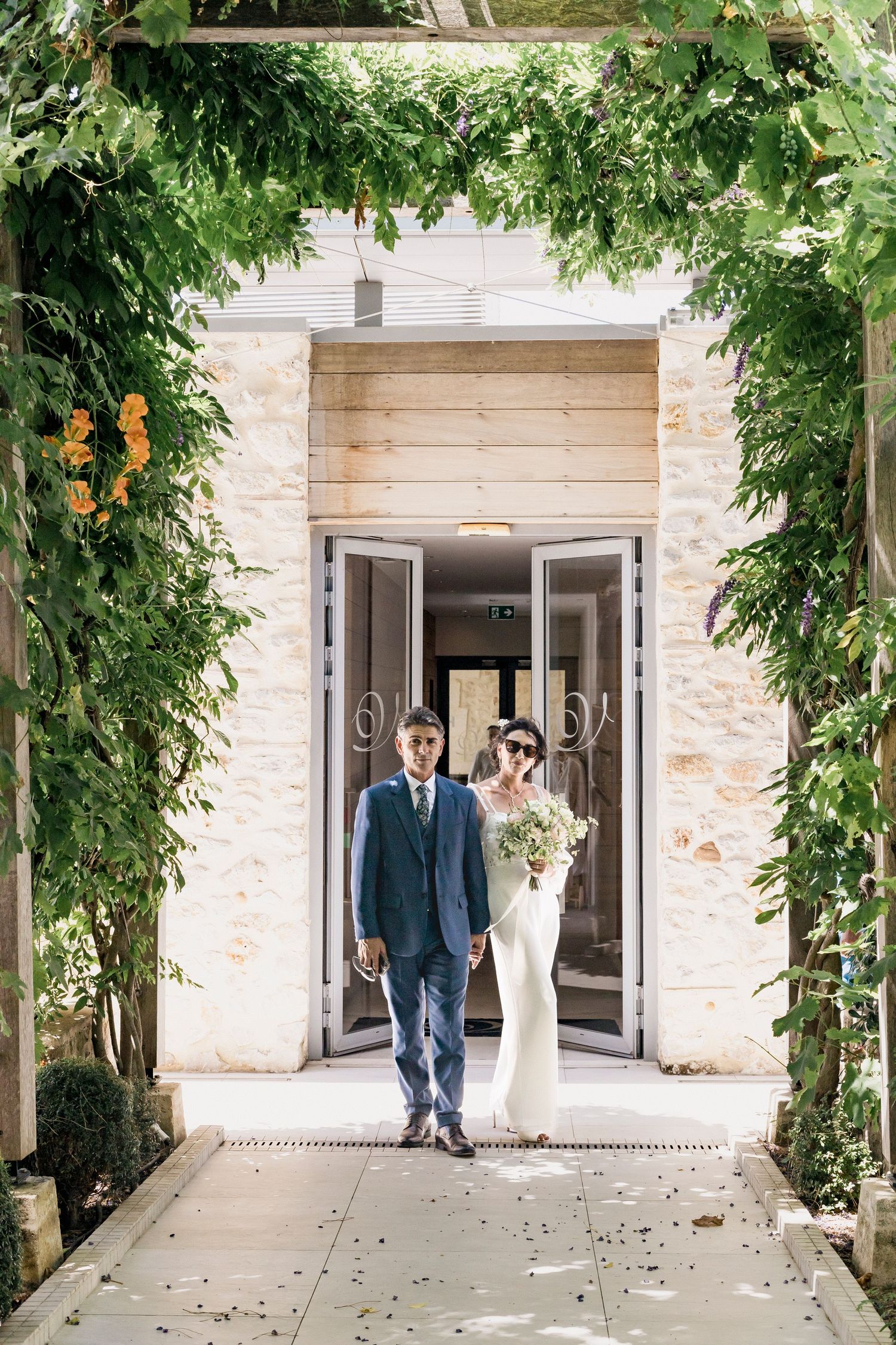 Wedding couple photographed in sequence walking through elegant stone archway with greenery.