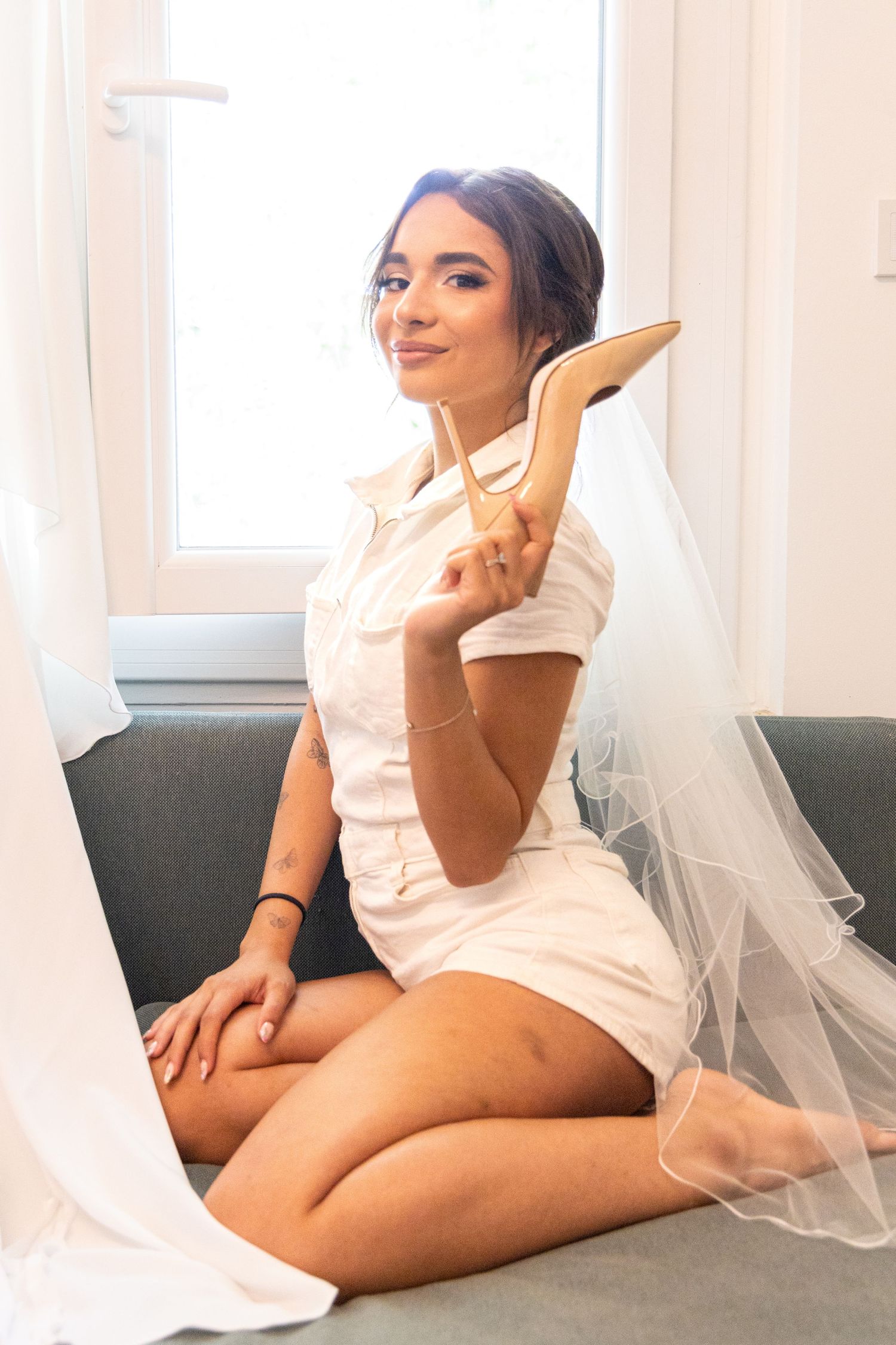 Bride in white robe posing on couch during wedding morning preparations.
