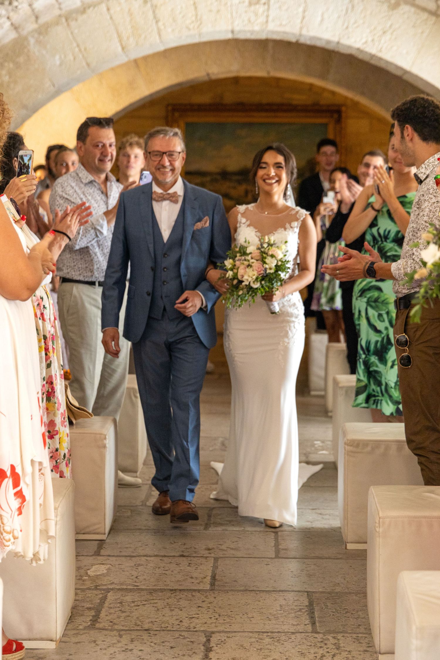 Wedding guests in colorful attire applaud during a celebration in a stone archway.
