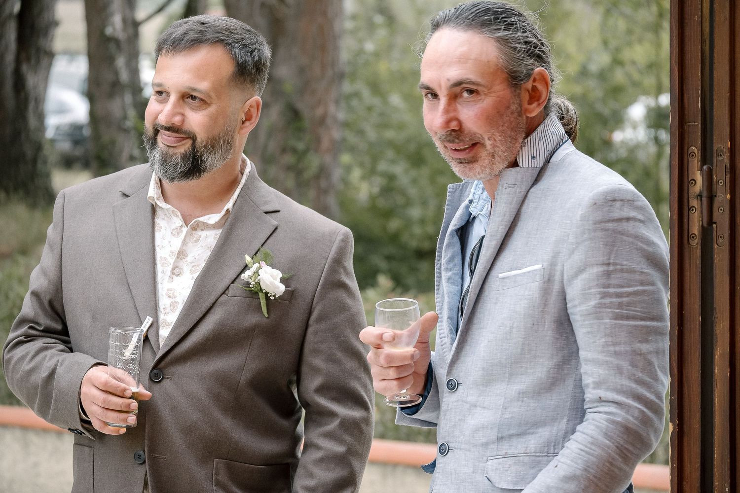 Groomsmen in grey suits sharing drinks and laughs during wedding celebration.