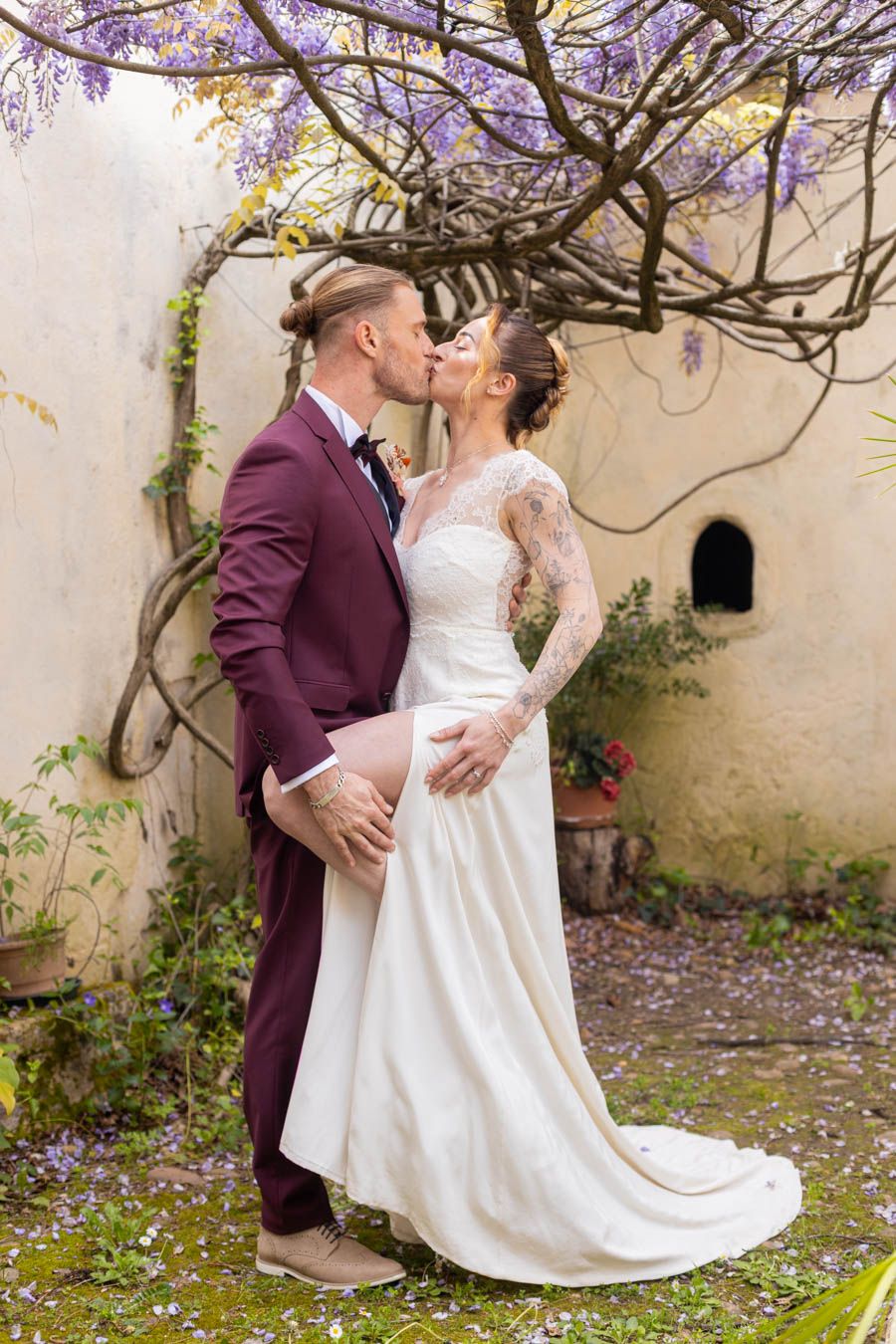 Romantic garden wedding photos with couple dancing under blooming wisteria and stone wall backdrop.