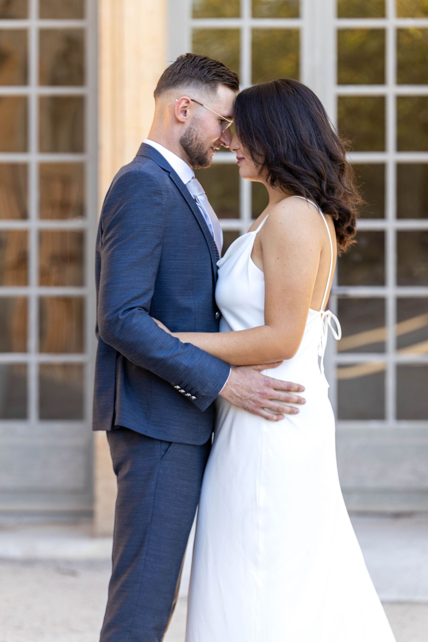 Wedding couple embracing outside elegant building with white window panes.