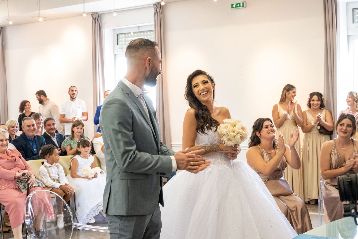 Newlyweds celebrate during their wedding ceremony surrounded by guests in a bright indoor venue.