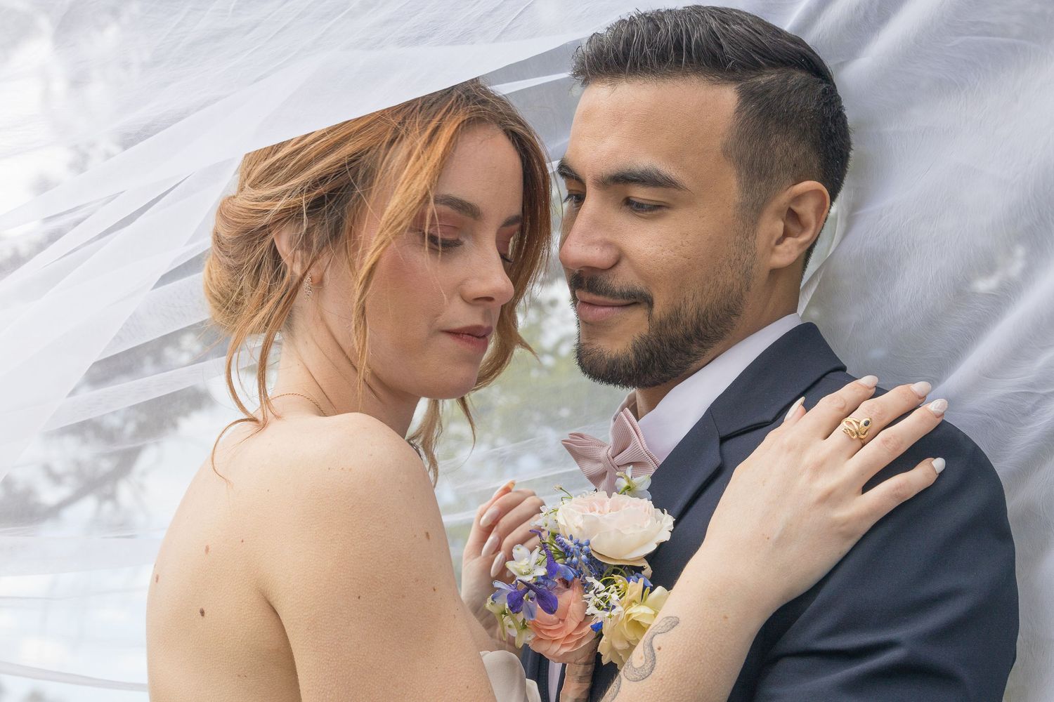 Dreamy wedding portrait with couple embracing under soft white veil.
