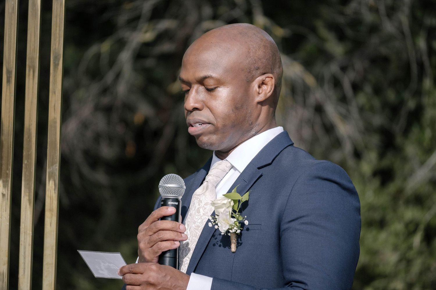 A groom reads from notes while speaking at outdoor wedding ceremony.