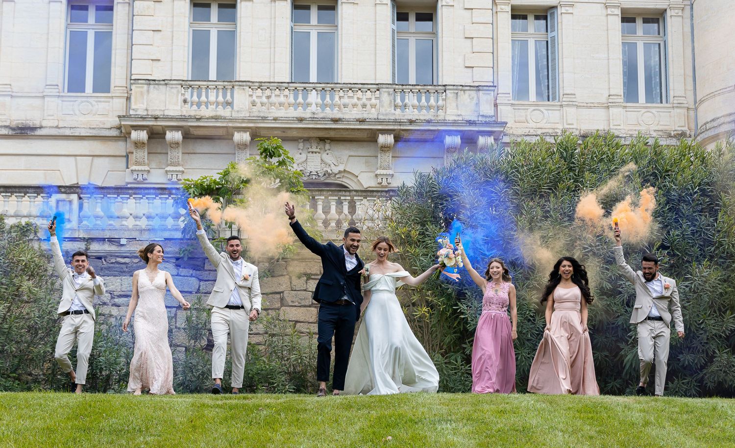 Wedding party lined up for formal group photo in front of elegant building facade.