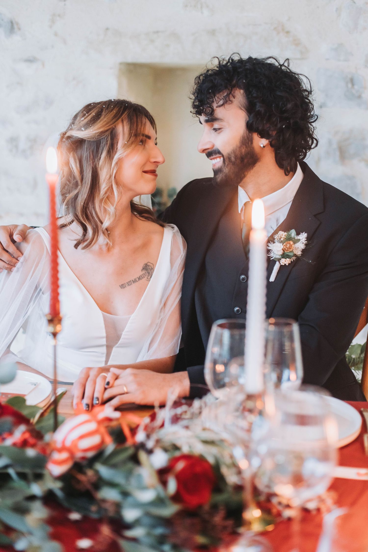 Intimate moment between newlyweds at rustic stone wall reception setting with candlelit table.