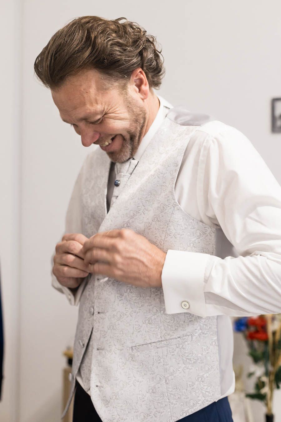 Groom adjusting white textured formal vest while getting dressed.