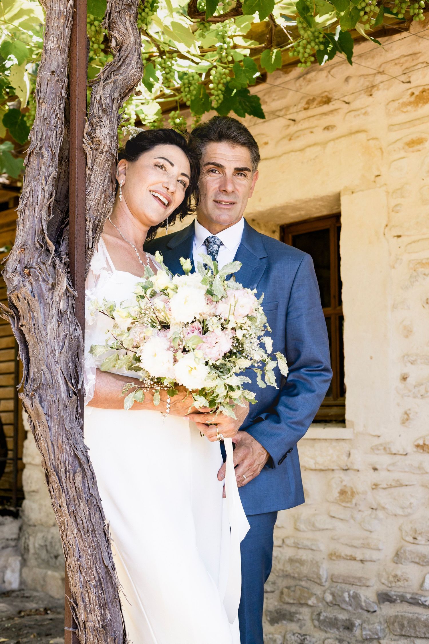 Romantic wedding portraits featuring a white dress and blue suit against a stone wall backdrop.