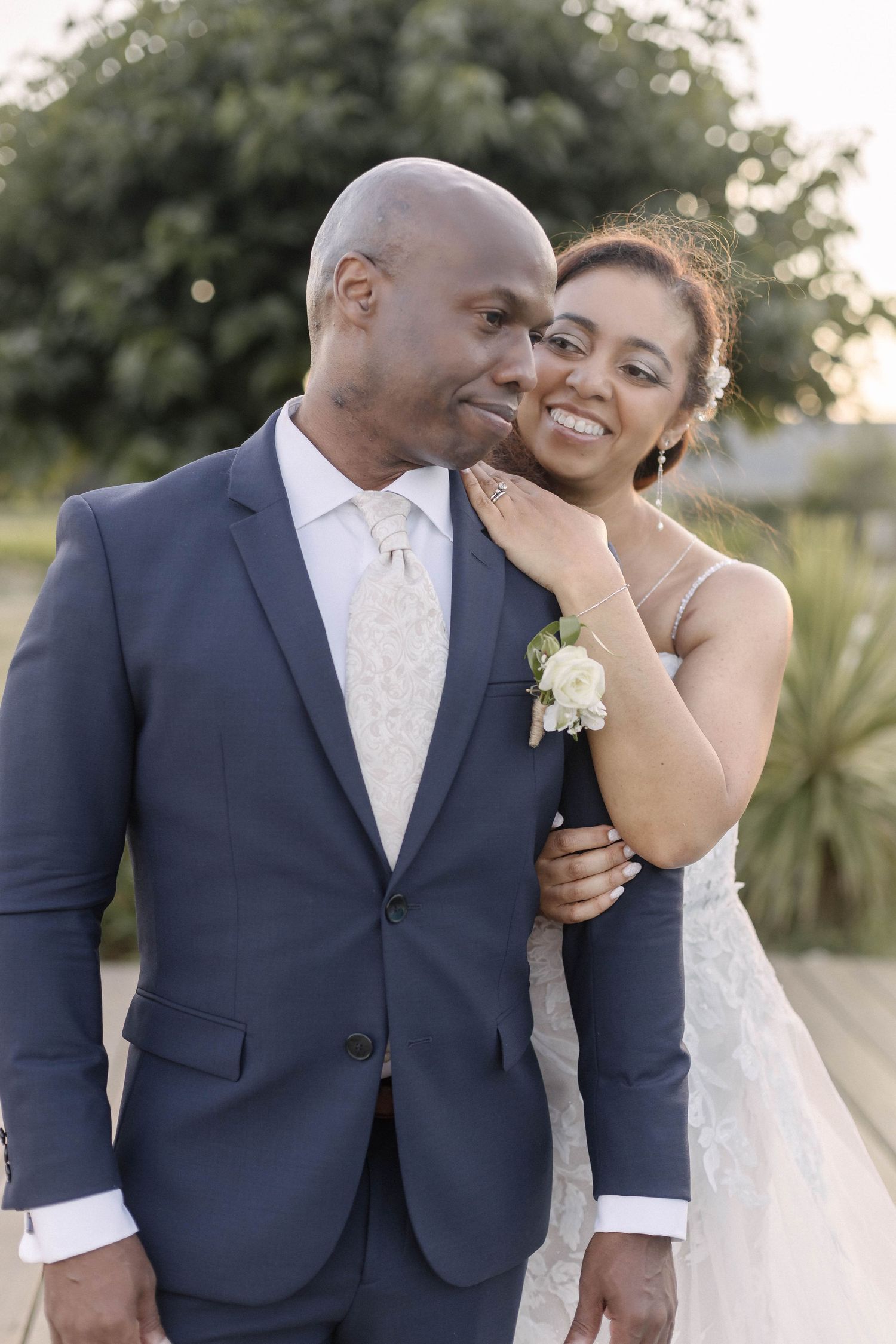 A joyful wedding couple shares romantic moments outdoors wearing navy suit and white gown.