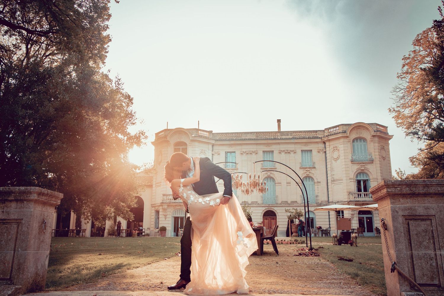 Panoramic wedding venue shot at sunset with elegant architecture and silhouetted figures.